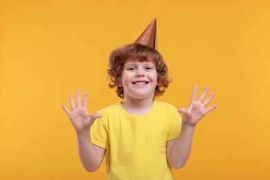 Photo of Happy little boy in party hat on orange background