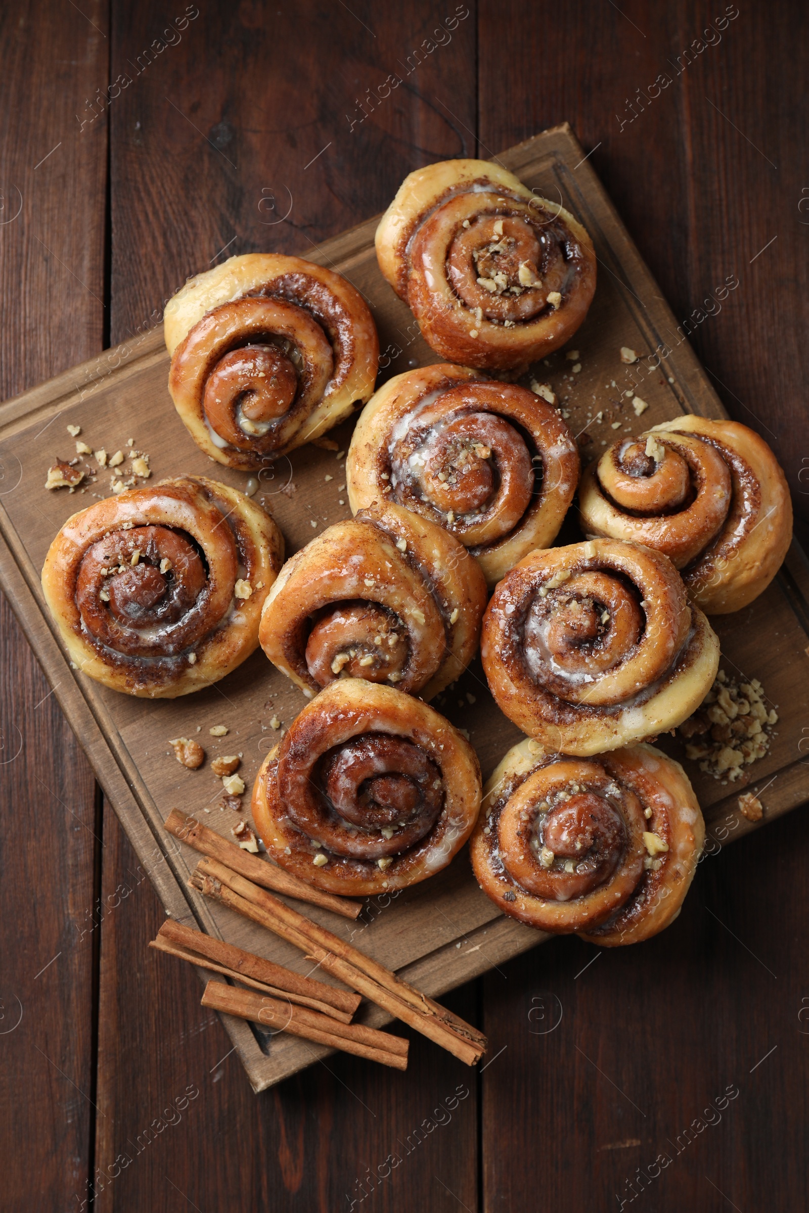 Photo of Tasty cinnamon rolls, sticks and nuts on wooden table, top view