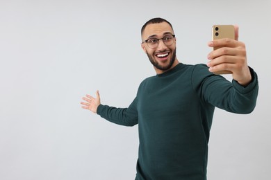 Photo of Smiling young man taking selfie with smartphone on grey background, space for text