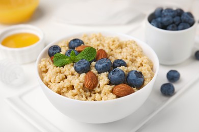 Photo of Bowl of delicious cooked quinoa with almonds and blueberries on white table, closeup