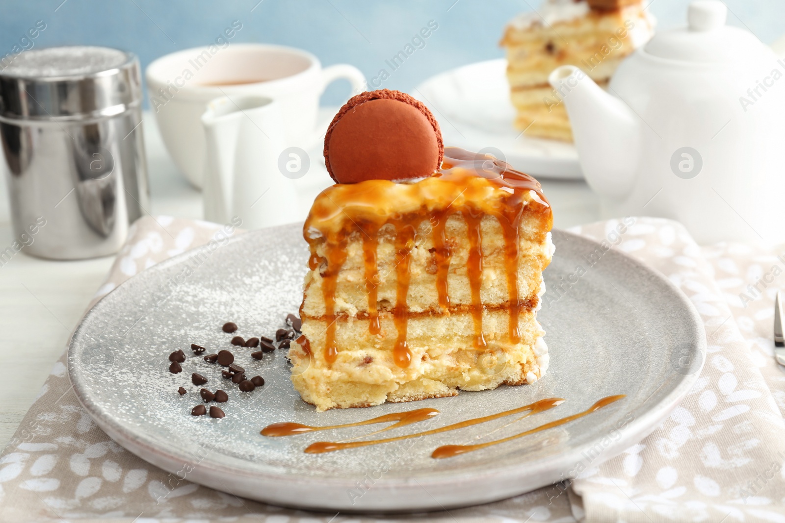 Photo of Piece of delicious homemade cake with caramel sauce and macaron on table