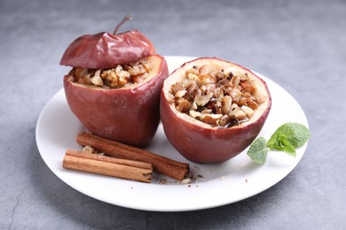 Photo of Tasty baked apples with nuts, honey, cinnamon sticks and mint on gray table