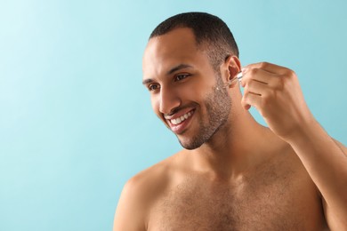 Photo of Handsome man applying cosmetic serum onto face on light blue background, space for text