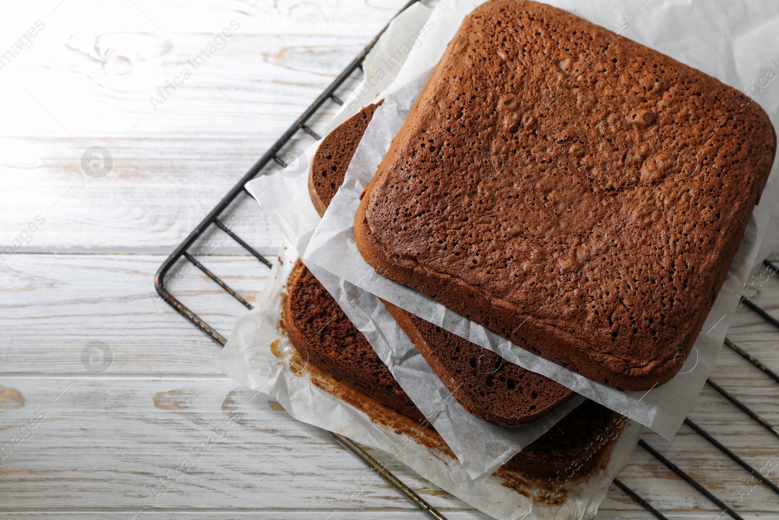 Photo of Layers of homemade chocolate sponge cake on white wooden table. Space for text