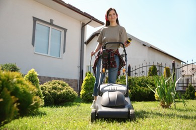 Smiling woman with modern lawn mower in garden, low angle view