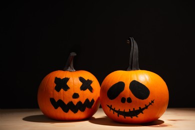 Photo of Halloween pumpkins with drawn faces on wooden table against black background, space for text