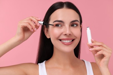 Photo of Beautiful woman applying serum onto her eyelashes on pink background. Cosmetic product