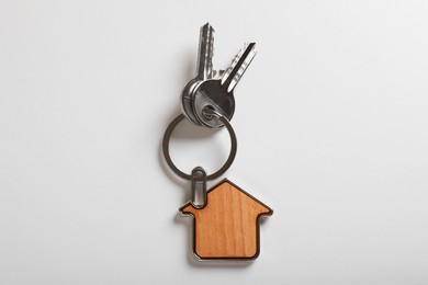 Keys with trinket in shape of house on white background, top view. Real estate agent services