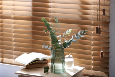 Vase with fresh eucalyptus branches on table near window in room. Interior design