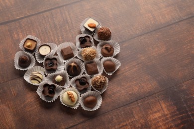 Photo of Heart made with delicious chocolate candies on wooden table. Space for text