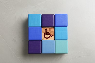 Image of Inclusion concept. Wooden cube with international symbol of access among colorful ones on light background, top view