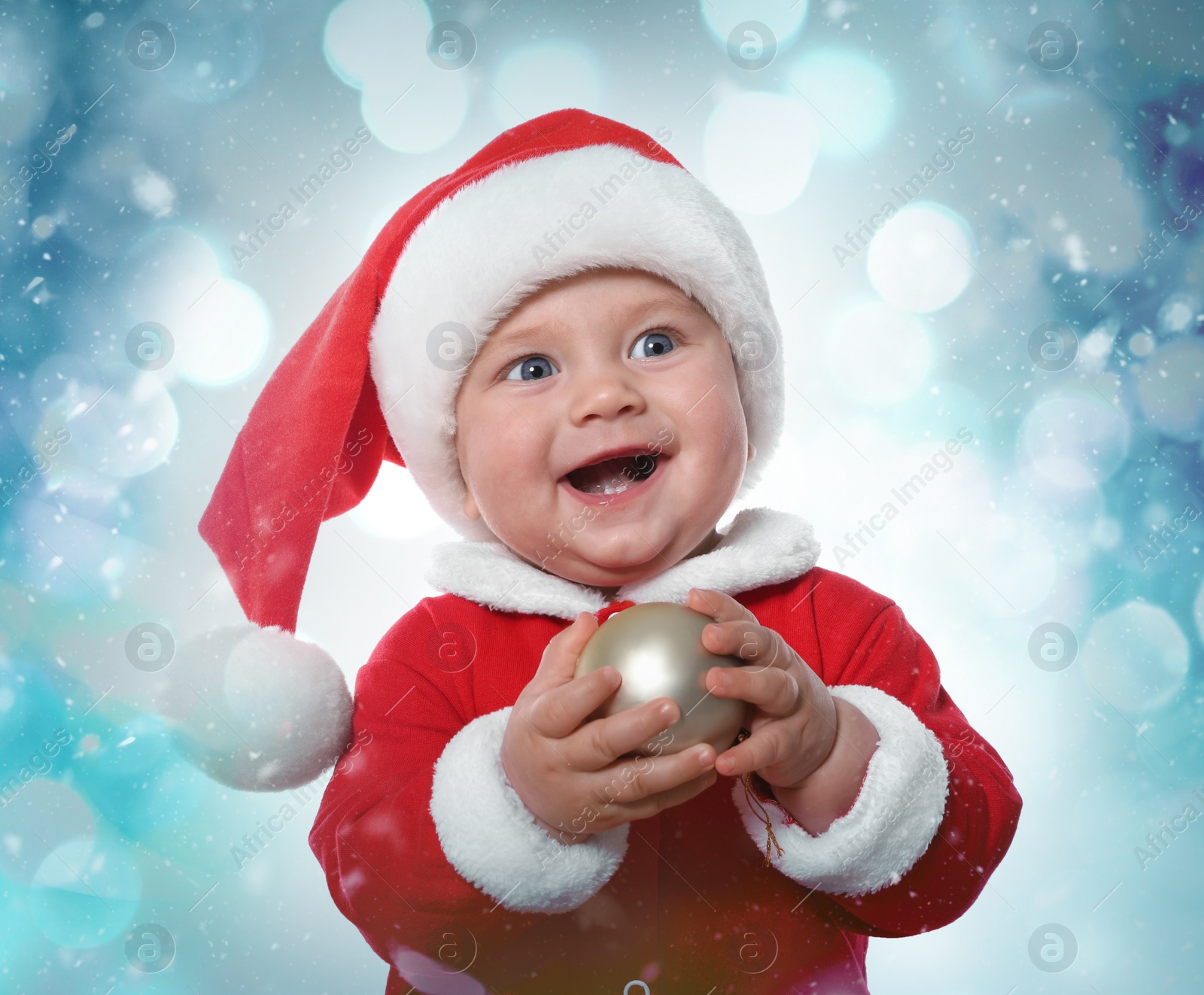 Image of Cute baby in costume with Christmas ball against blurred festive lights 