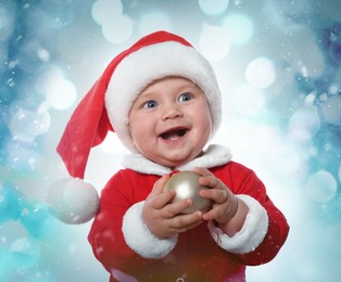 Cute baby in costume with Christmas ball against blurred festive lights 