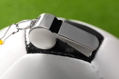 Photo of Football referee equipment. Soccer ball and metal whistle on green background, closeup