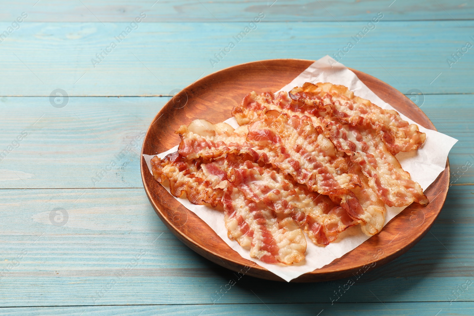 Photo of Delicious fried bacon slices on blue wooden table. Space for text