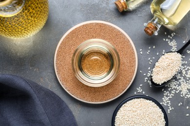 Sesame oil and seeds on grey table, flat lay