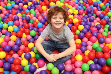 Photo of Happy little boy sitting on colorful balls in ball pit