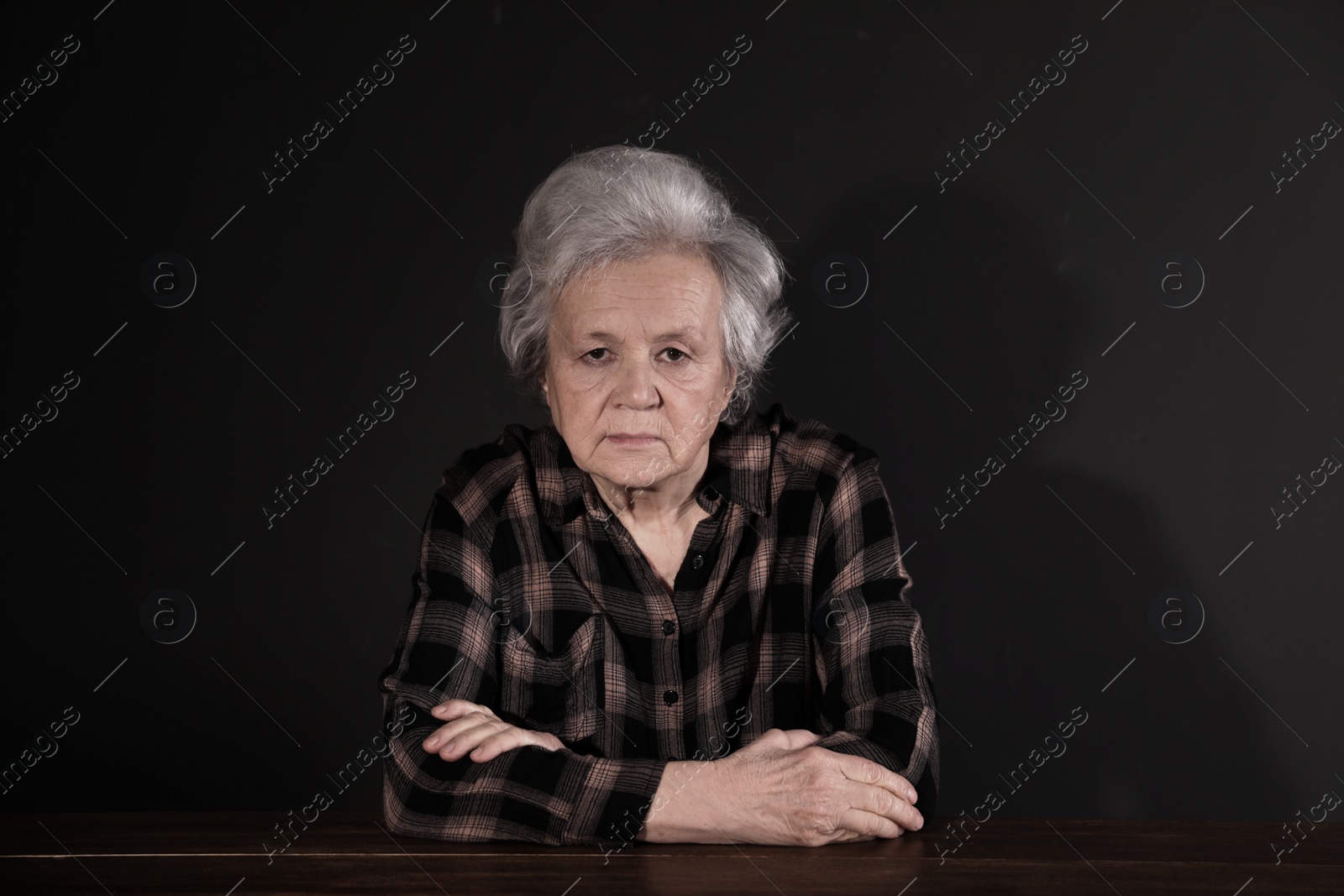 Photo of Poor upset woman sitting at table on dark background