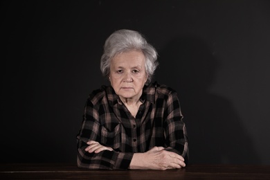 Poor upset woman sitting at table on dark background