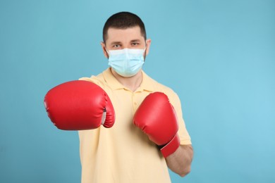 Photo of Man with protective mask and boxing gloves on light blue background. Strong immunity concept