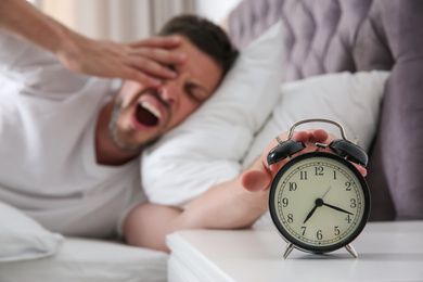 Sleepy man turning off alarm clock at home in morning, focus on hand