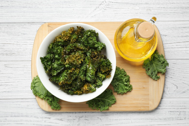 Tasty baked kale chips on white wooden table, top view