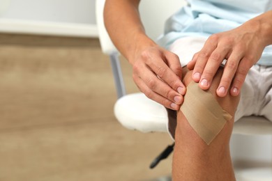 Man putting sticking plaster onto knee indoors, closeup. Space for text