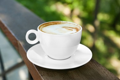 Photo of Cup of aromatic coffee on wooden railing outdoors