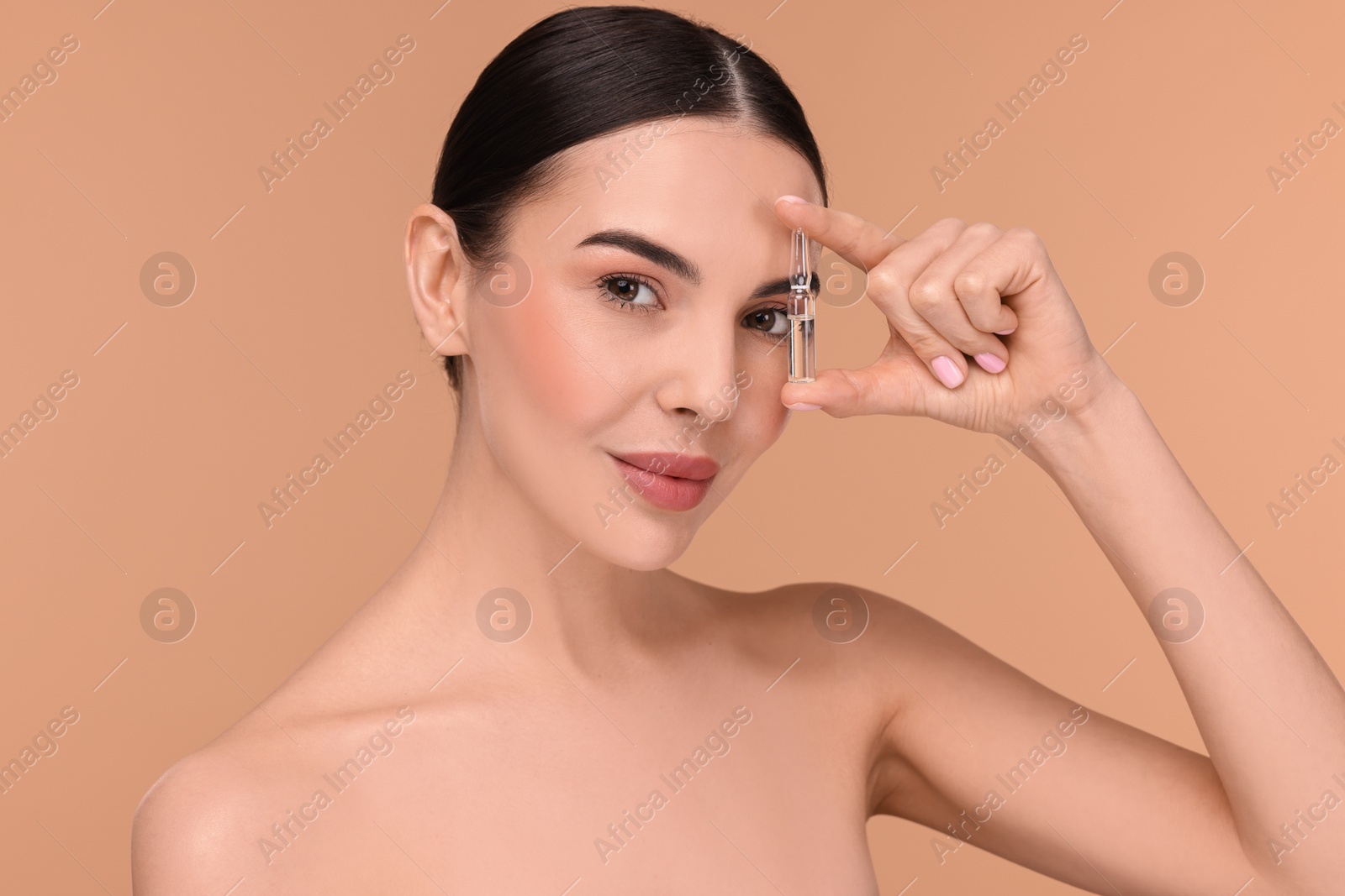 Photo of Beautiful young woman holding skincare ampoule on beige background