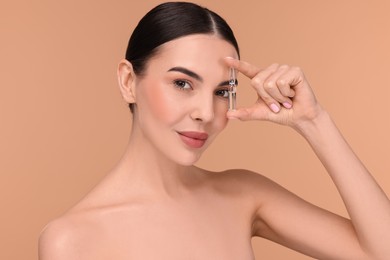 Beautiful young woman holding skincare ampoule on beige background