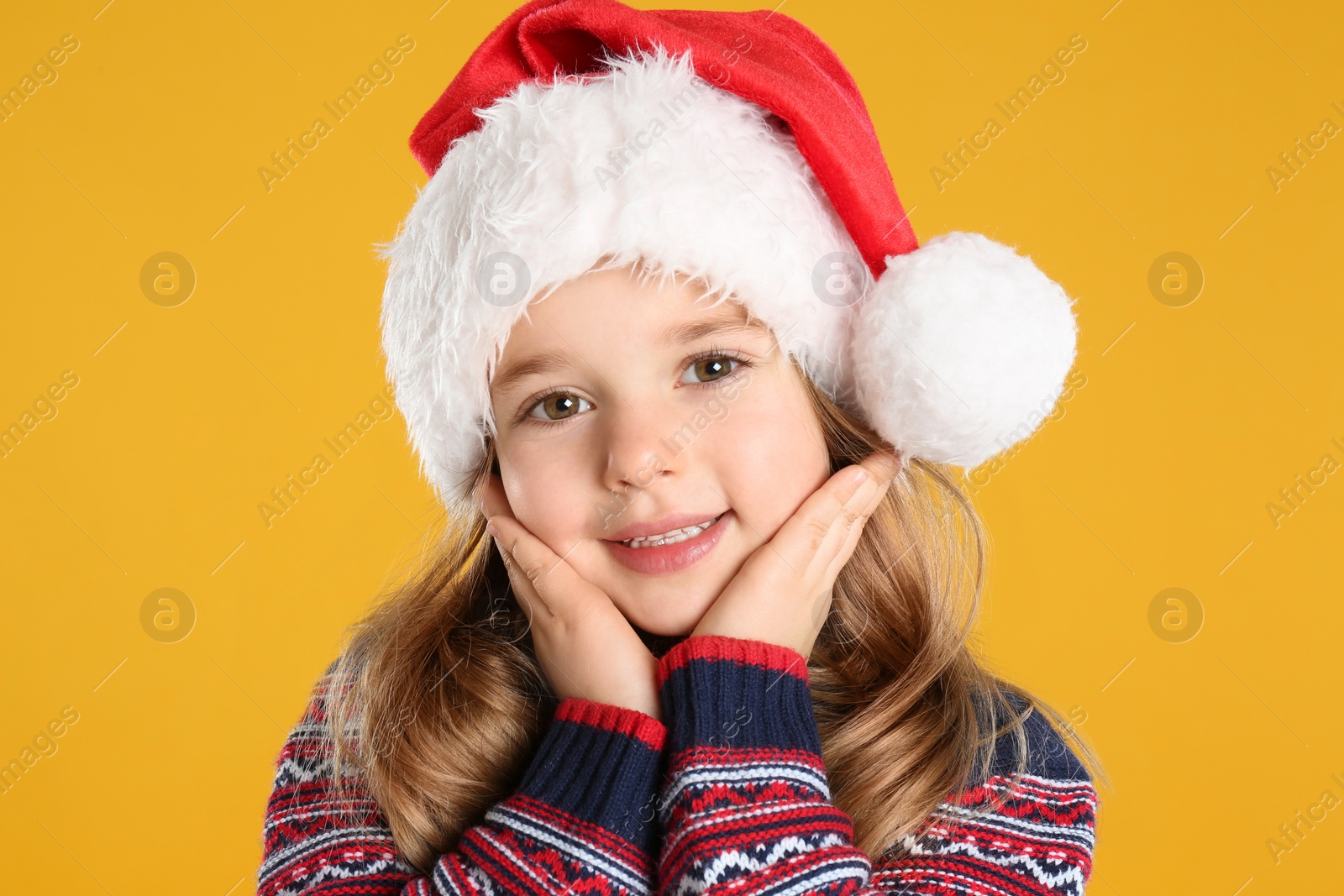 Photo of Cute child in Santa hat on yellow background. Christmas celebration