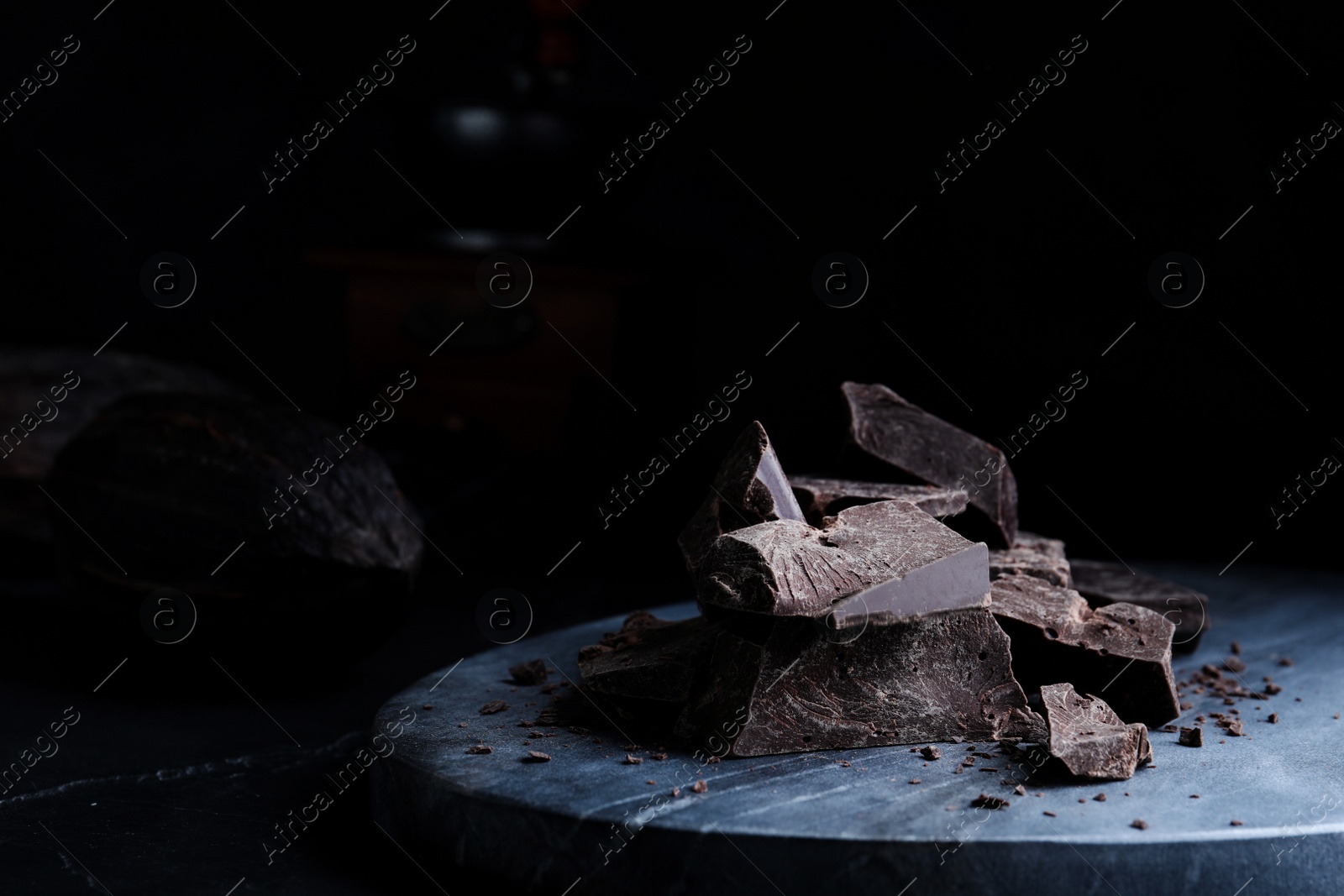 Photo of Pieces of tasty dark chocolate on grey marble board, closeup