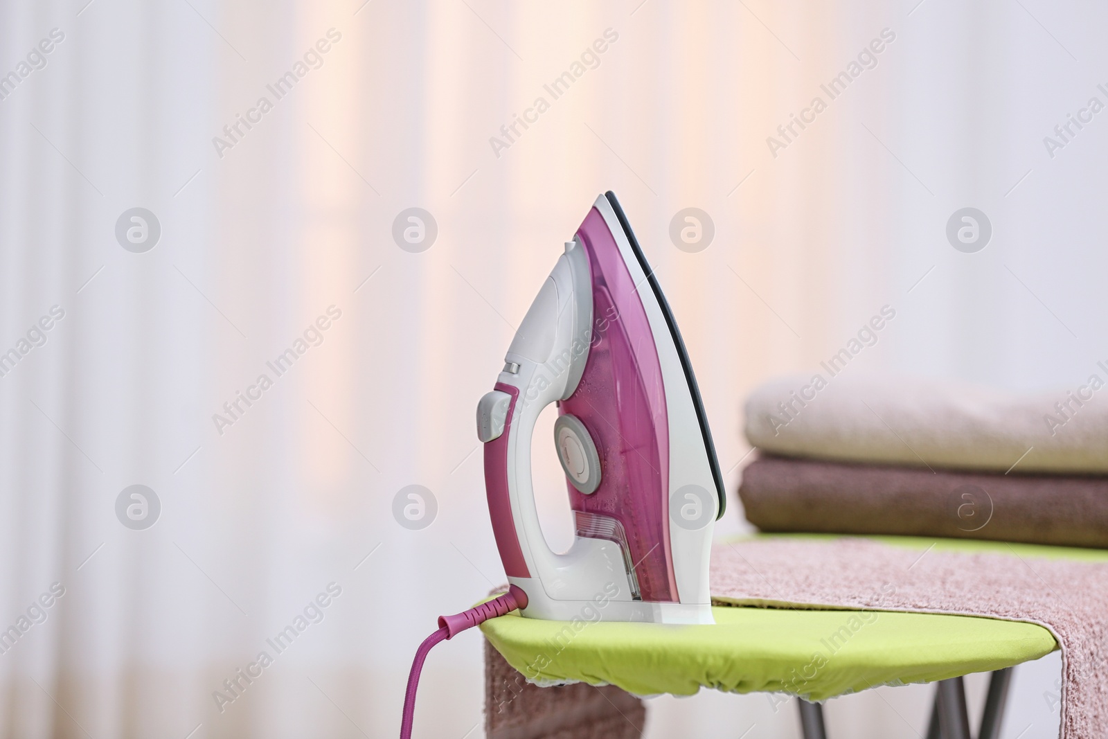 Photo of Modern iron and towels on board against blurred background. Space for text