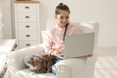 Photo of Cute little girl with laptop and cat in armchair at home. First pet
