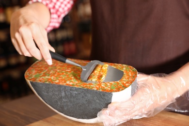 Seller slicing delicious cheese on table in store