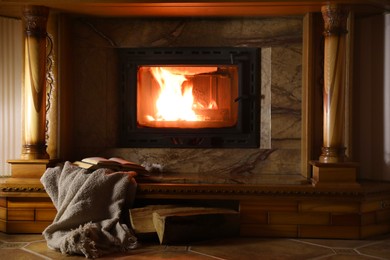 Blanket, books and firewood near fireplace at home