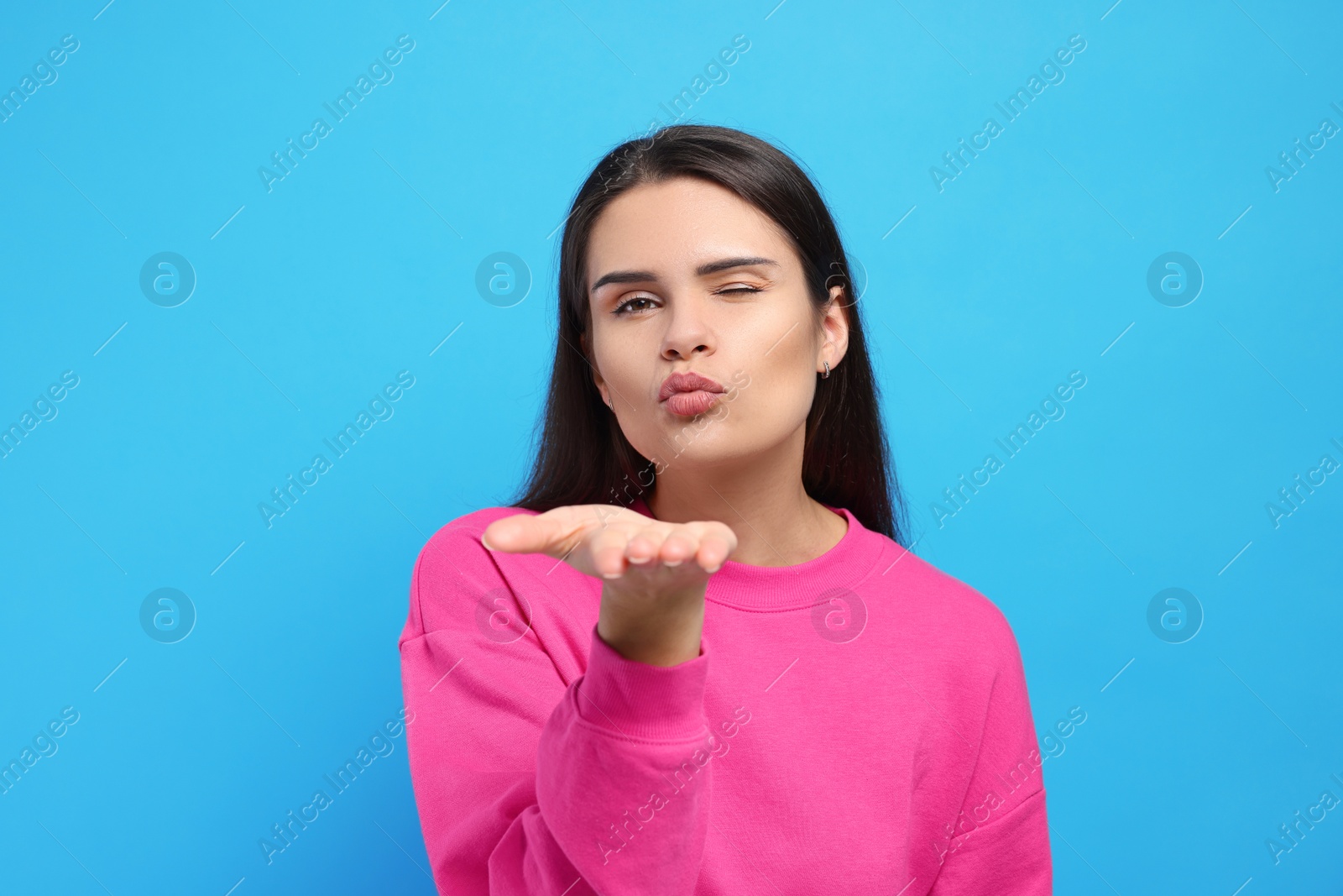 Photo of Beautiful young woman blowing kiss on light blue background