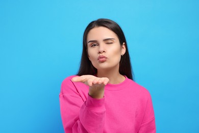 Beautiful young woman blowing kiss on light blue background