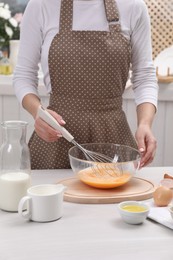 Photo of Woman whisking eggs in bowl at table indoors, closeup