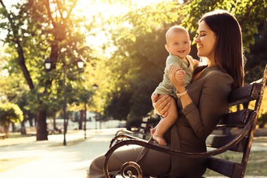 Photo of Young mother with her cute baby on bench in park