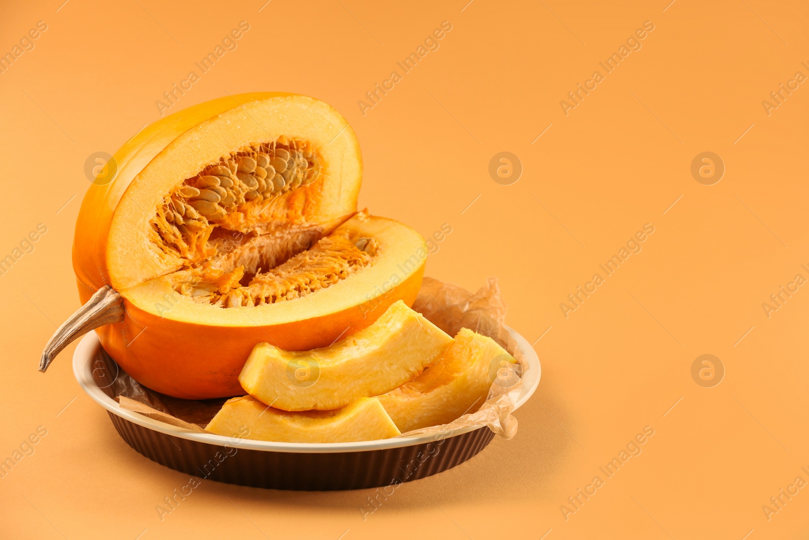 Photo of Cut fresh ripe pumpkin on pale orange background, space for text
