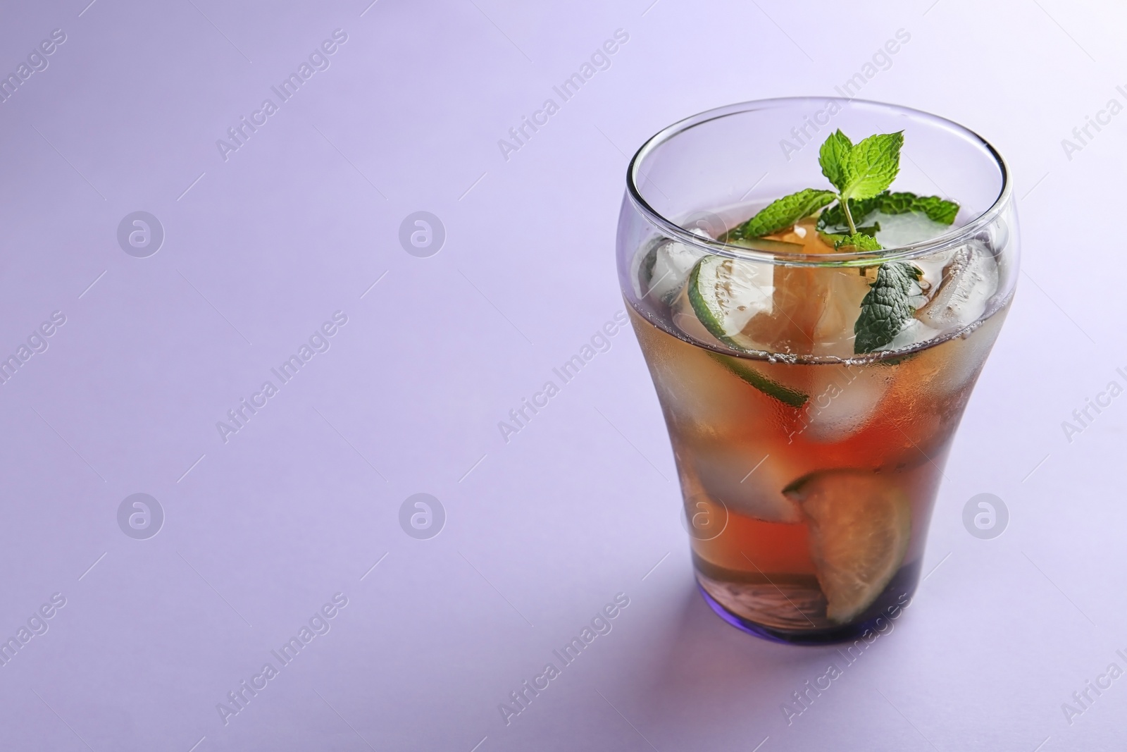 Photo of Glass of refreshing iced tea on lilac background. Space for text