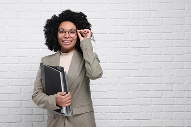 Photo of Young businesswoman with folders near white brick wall. Space for text