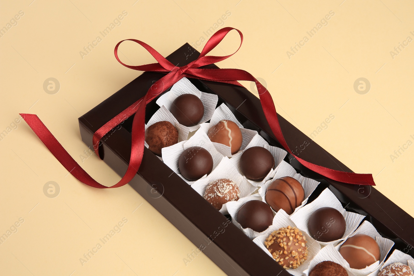Photo of Box with delicious chocolate candies on beige table, closeup