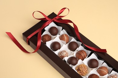 Photo of Box with delicious chocolate candies on beige table, closeup