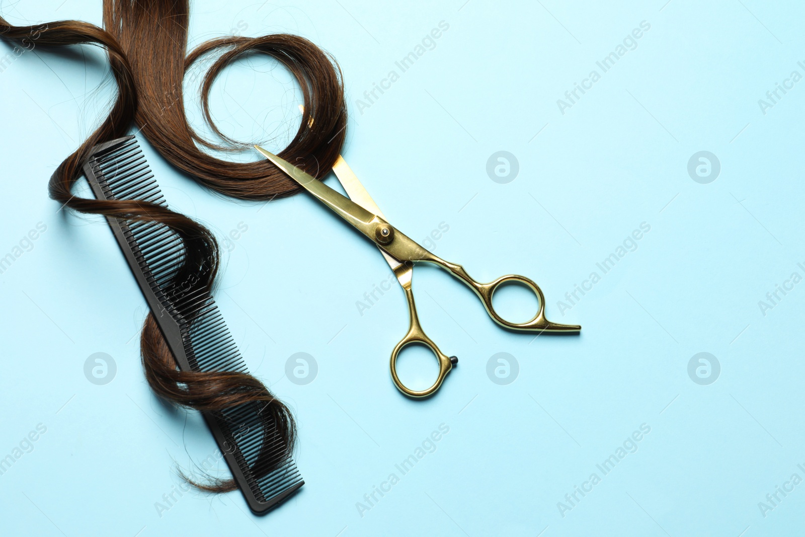 Photo of Professional hairdresser scissors and comb with brown hair strand on light blue background, flat lay. Space for text