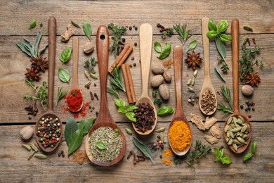 Different herbs and spices with spoons on wooden table, flat lay