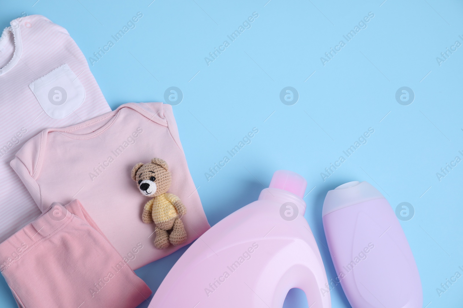 Photo of Bottles of laundry detergents, baby clothes and toy bear on light blue background, flat lay. Space for text