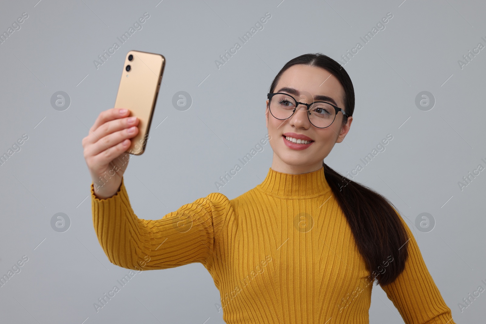 Photo of Smiling young woman taking selfie with smartphone on grey background