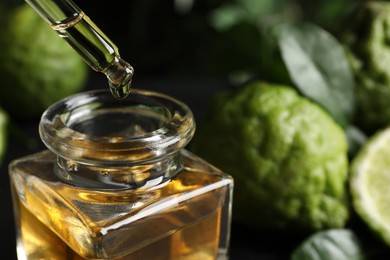 Photo of Dripping bergamot essential oil into glass bottle on black table, closeup